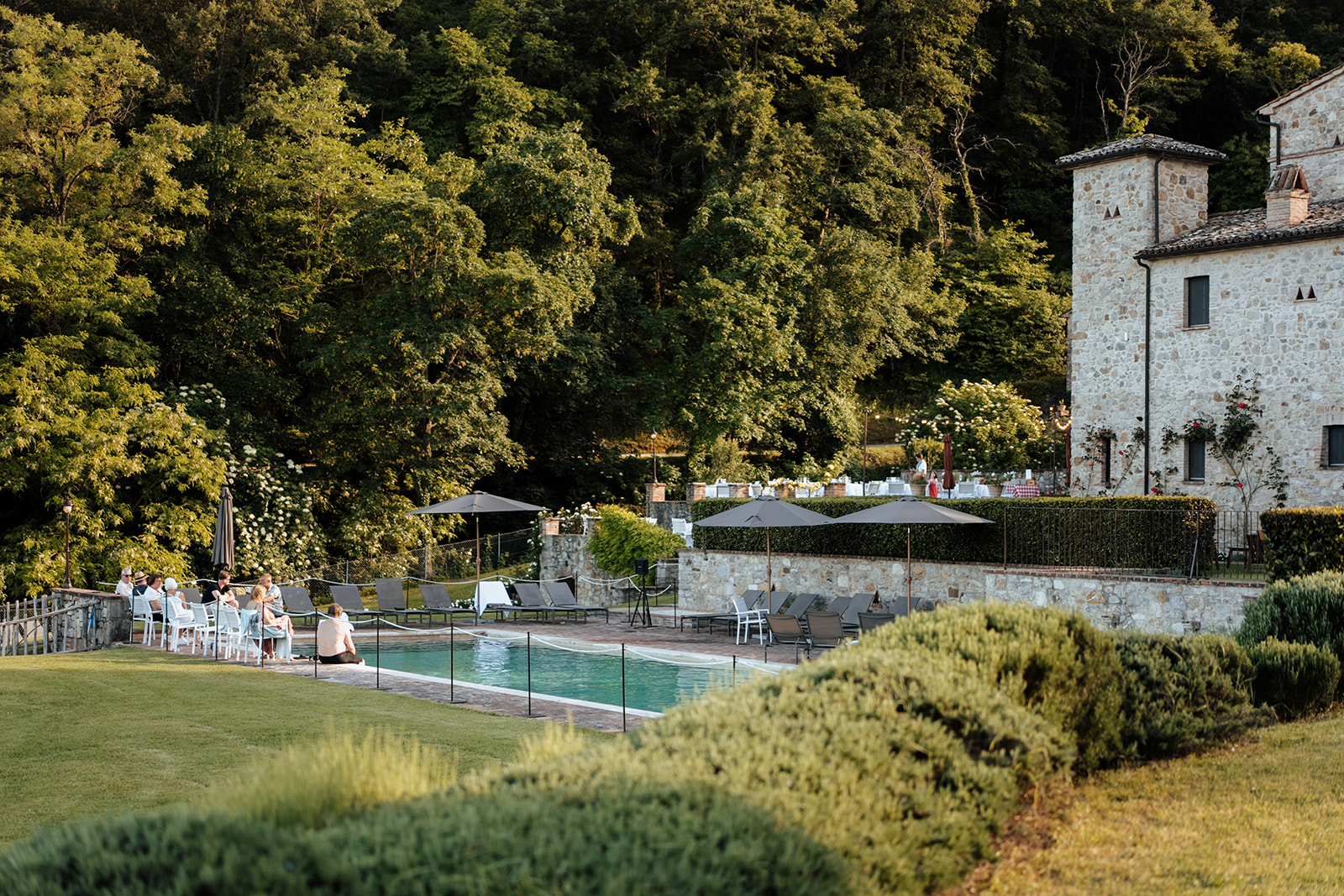 Guests gathered at the poolside lawn in golden evening light beside the stone tower