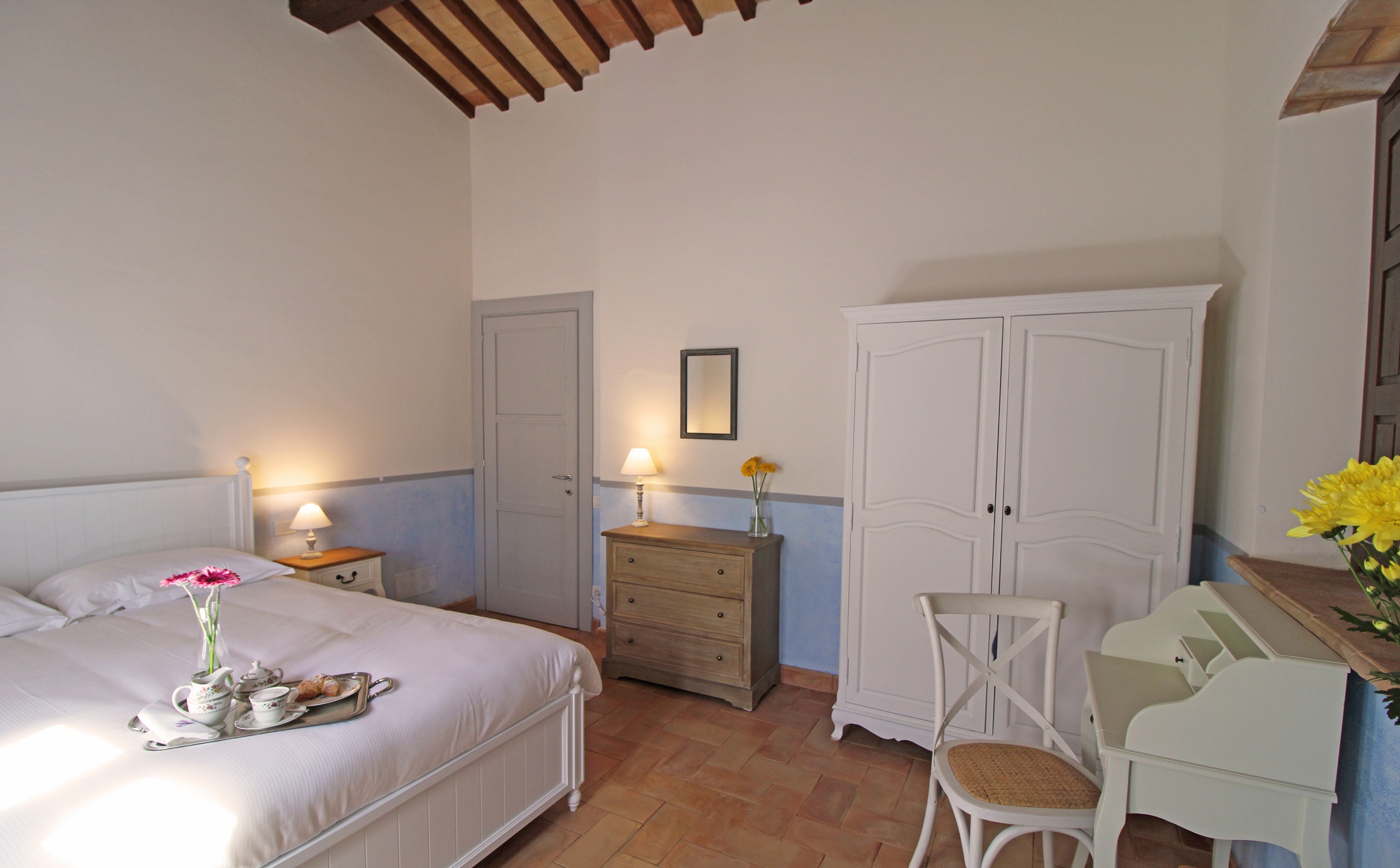 Bright bedroom with pale blue wall band, white armoire and a breakfast tray on the bed
