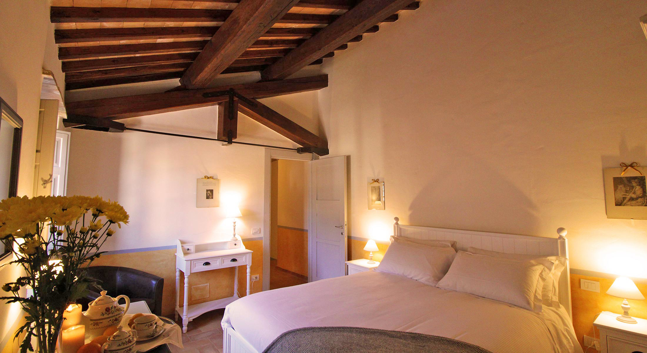 Warmly lit attic bedroom with exposed timber roof beams and lamps beside the bed