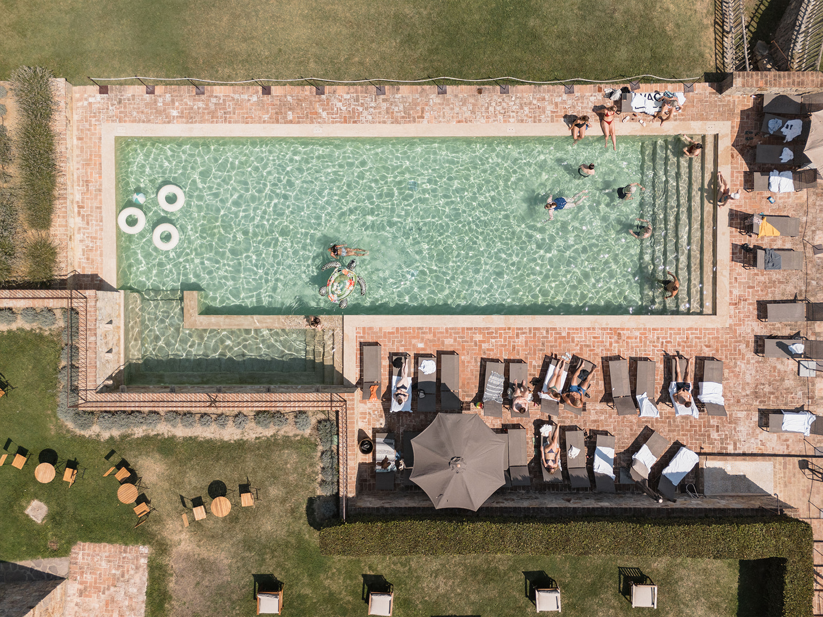 Overhead view of the long pool with swimmers, rings and rows of loungers on brick paving