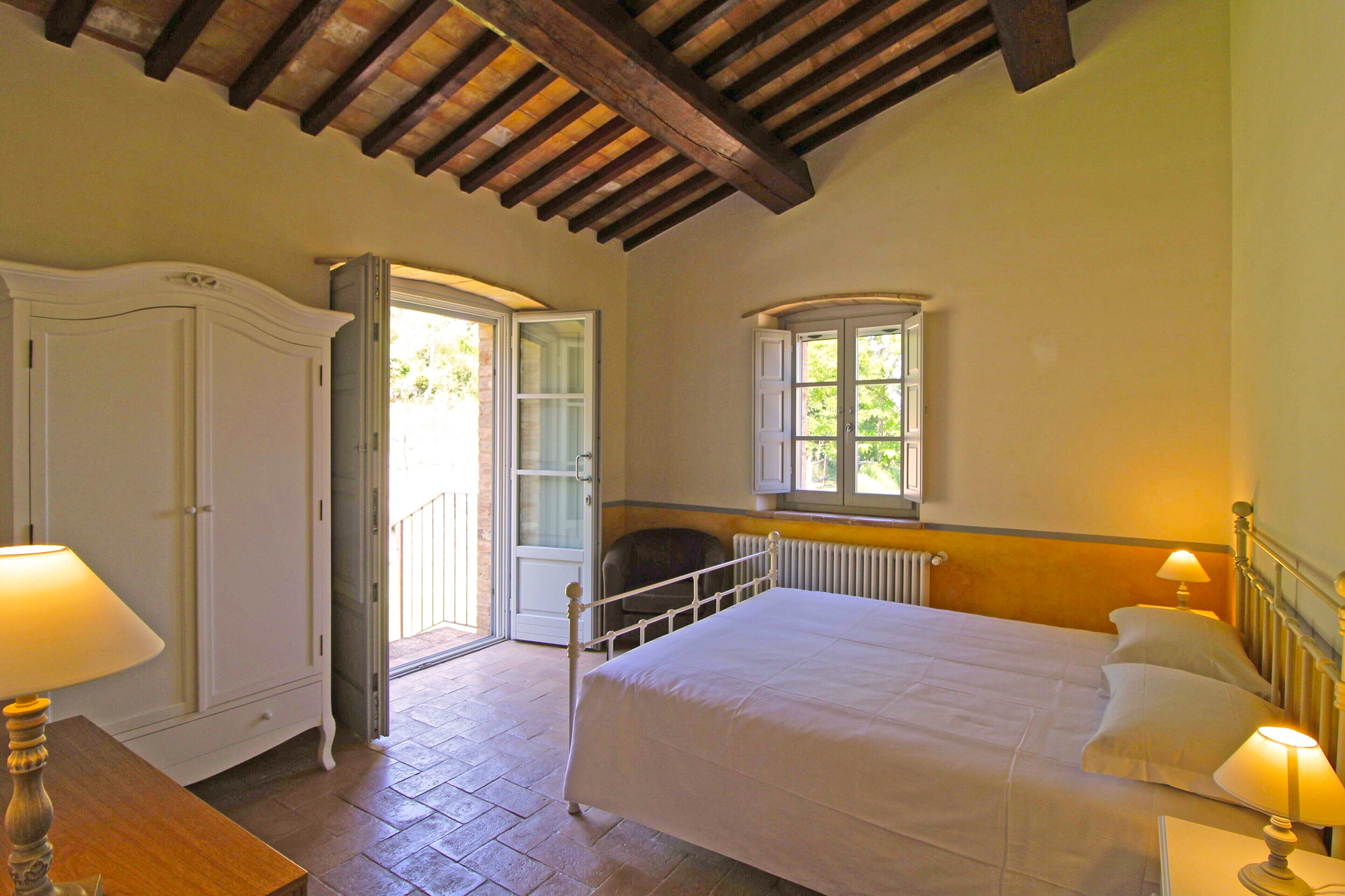 Suite with beamed ceiling, ochre wall band, brass bed and French doors onto a small balcony